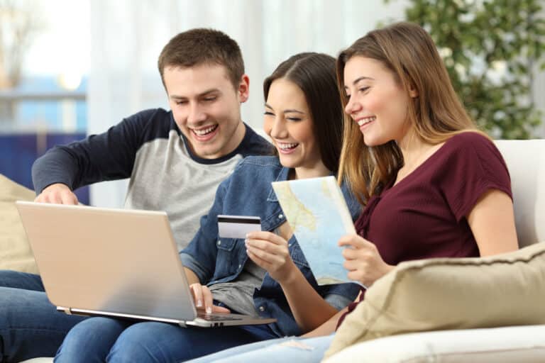 Trois amis préparent un voyage sur ordinateur avec une carte et une carte bancaire.