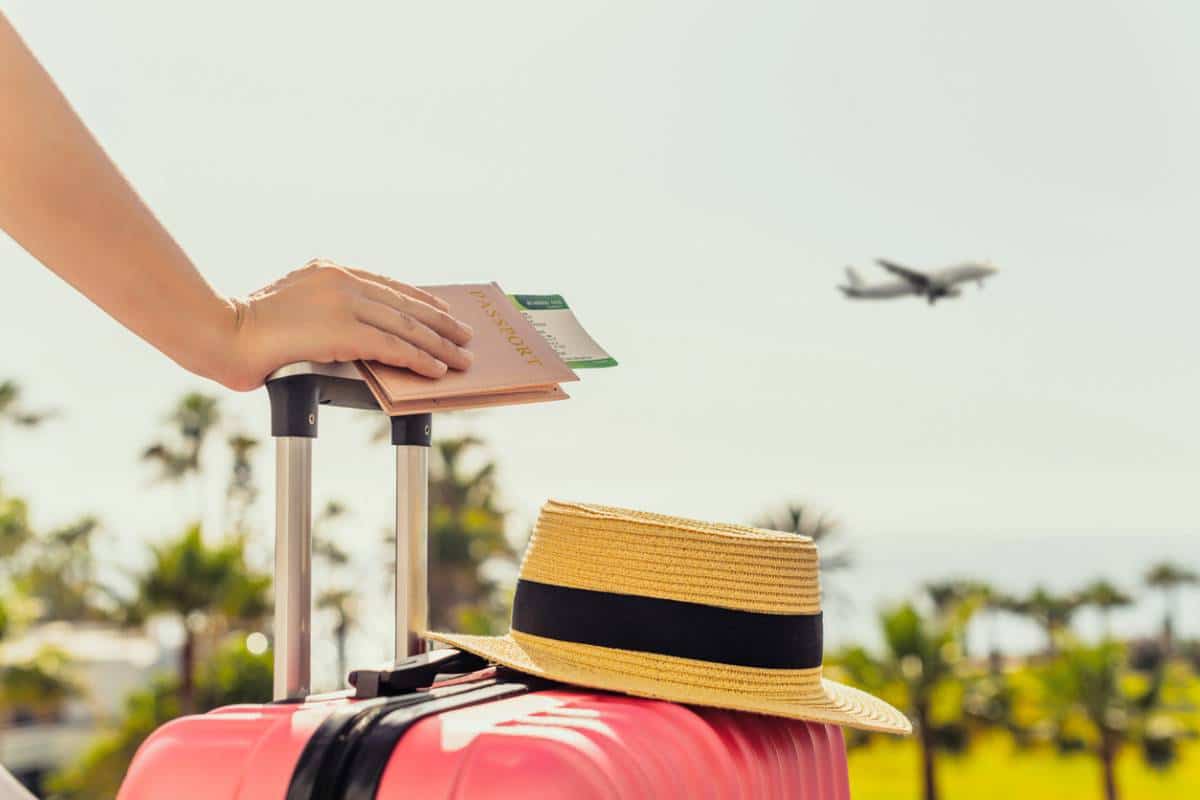 main tenant un passeport sur une valise rose avec un chapeau de paille et un avion en arrière-plan