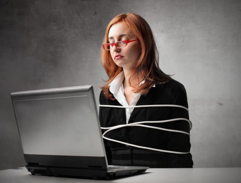 femme attachée avec un câble USB devant un ordinateur portable sur un fond gris.