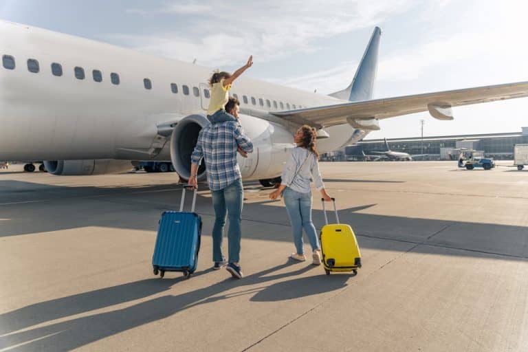 famille voyageant avec bagages à roulettes sur le tarmac devant un avion