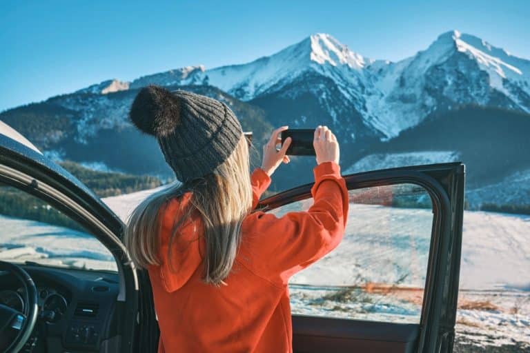 femme prenant photo de montagnes enneigées avec smartphone depuis une voiture