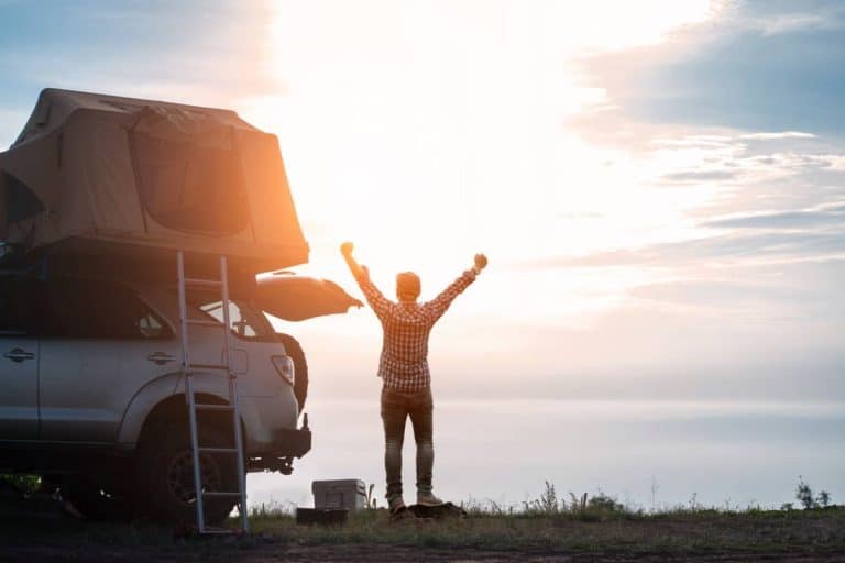 homme célébrant près de son SUV avec tente de toit au coucher de soleil