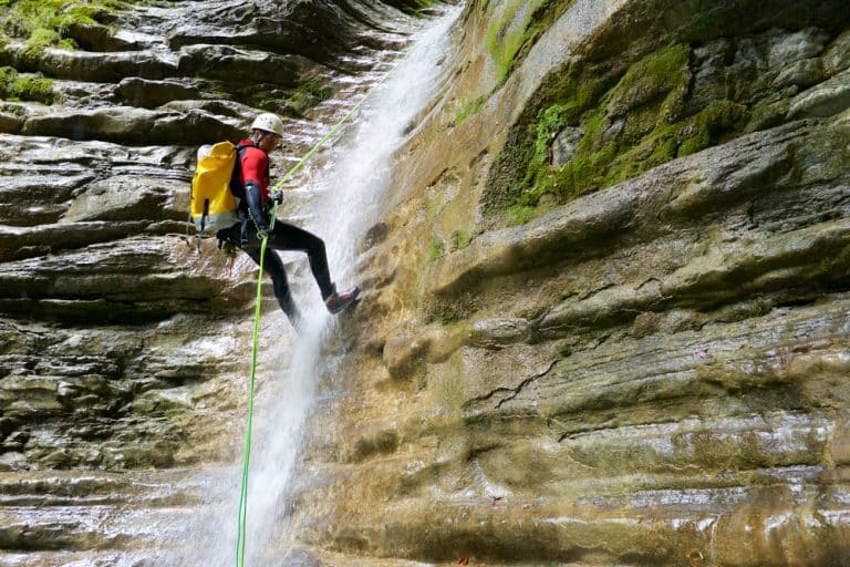 alpiniste effectuant du rappel sur une paroi rocheuse humide avec une cascade