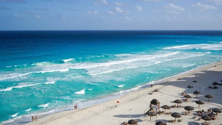 plage tropicale avec sable blanc, eau turquoise, parasols et visiteurs se détendant