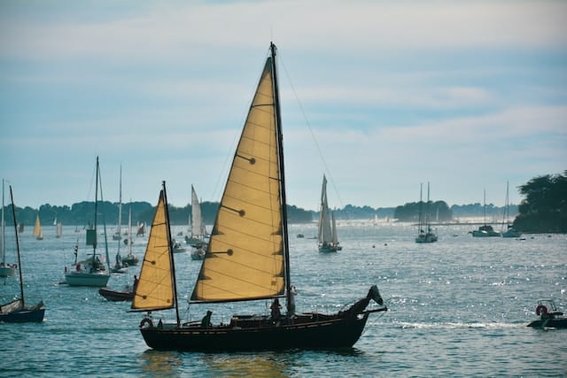 voiliers naviguant sur une eau calme avec des voiles jaunes et une lumière douce.