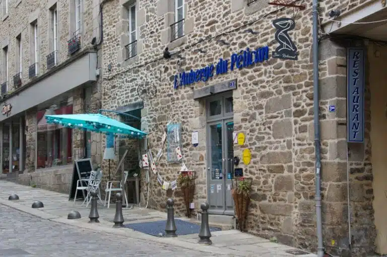 Stone facade restaurant with blue sign and outdoor seating in a quaint French street.