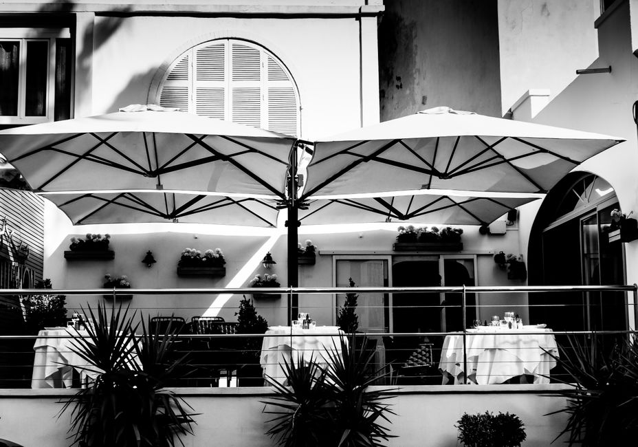 Charming black and white photo of an outdoor cafe in Antibes, France, featuring umbrellas and dining tables.