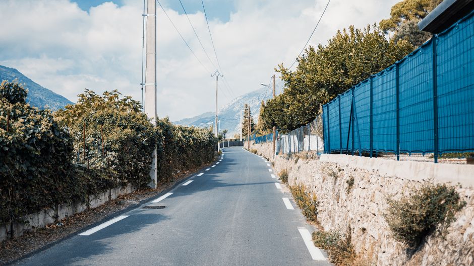 Serene view of a winding road lined with fences in Menton, France, under a bright day.