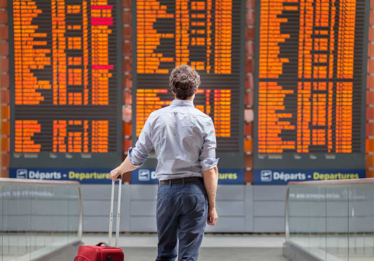 voyageur avec valise rouge devant tableau des départs d'aéroport