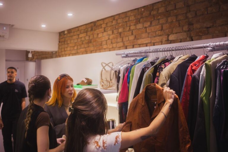 Three women browsing clothing in a stylish boutique with a man in the background.
