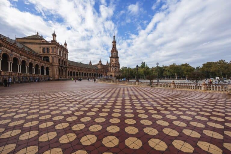Wide view of Plaza de España's iconic architecture with ceramic tiles and cloudy skies in Seville, Spain.