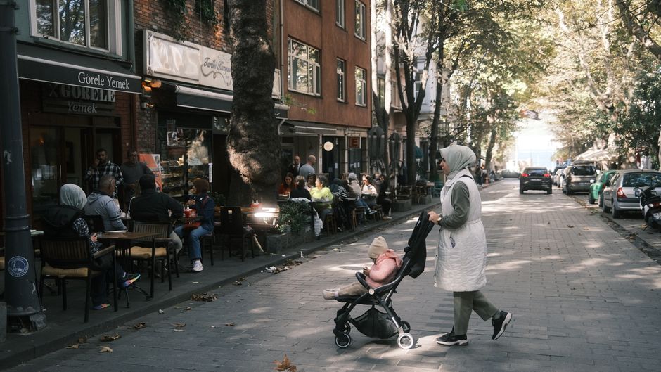 Urban street in İstanbul featuring pedestrians and outdoor cafes under autumn sunlight.